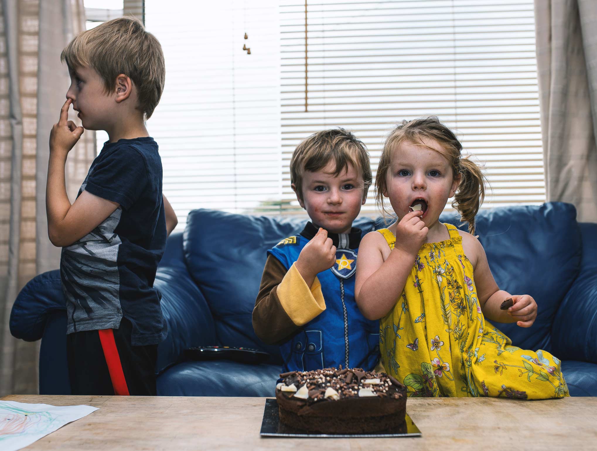 Three children at birthday eating chocolate and picking nose